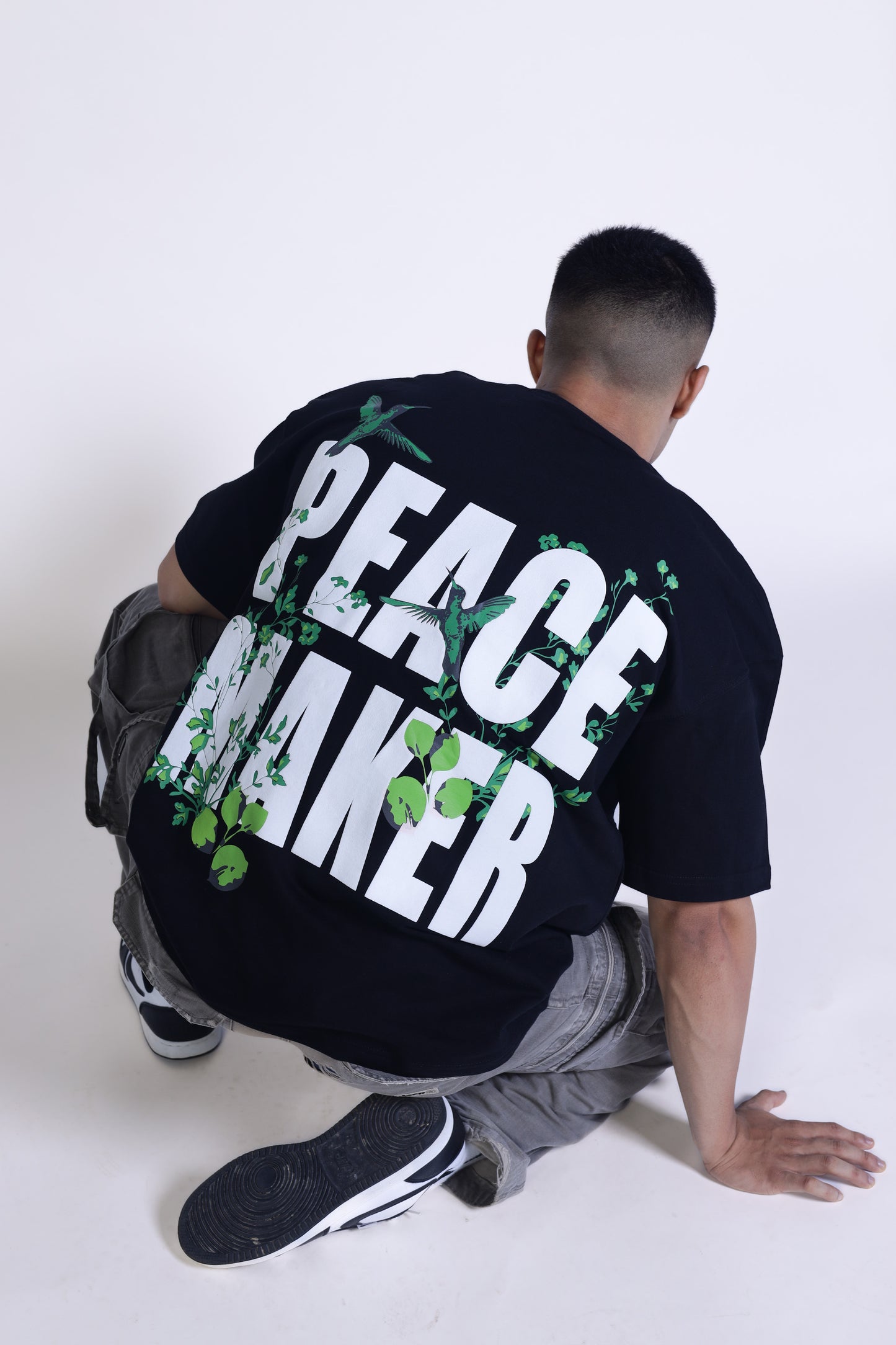 Man sitting and seeing in opposite direction wearing black oversized t-shirt peace maker written on it.