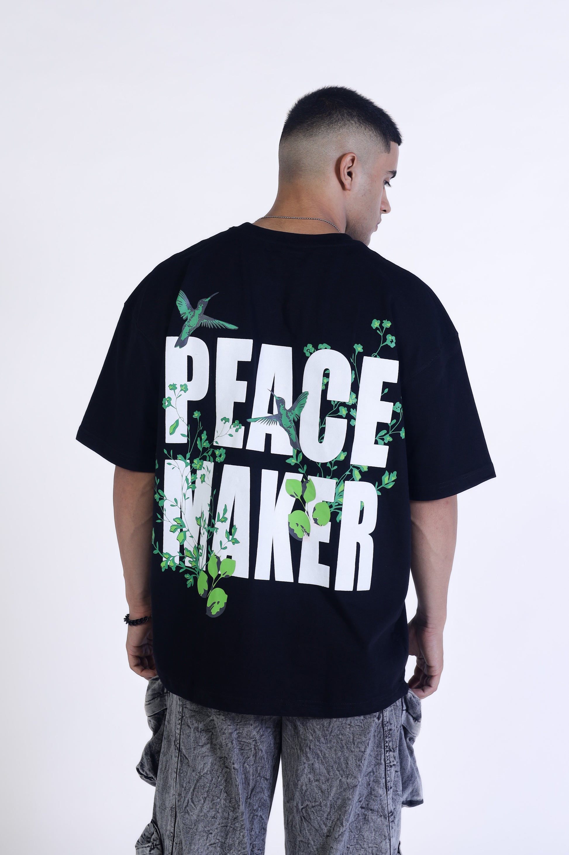 Man standing facing back wearing black t-shirt Peace Maker written on it